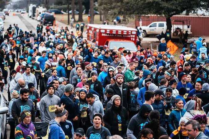 Hundreds of runners in hats and race bibs packed into the start corral, a Dallas Fire Rescue ambulance behind them