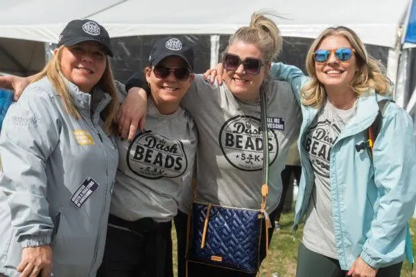 Four smiling volunteers in gray Dash for the Beads shirts outside the event tent
